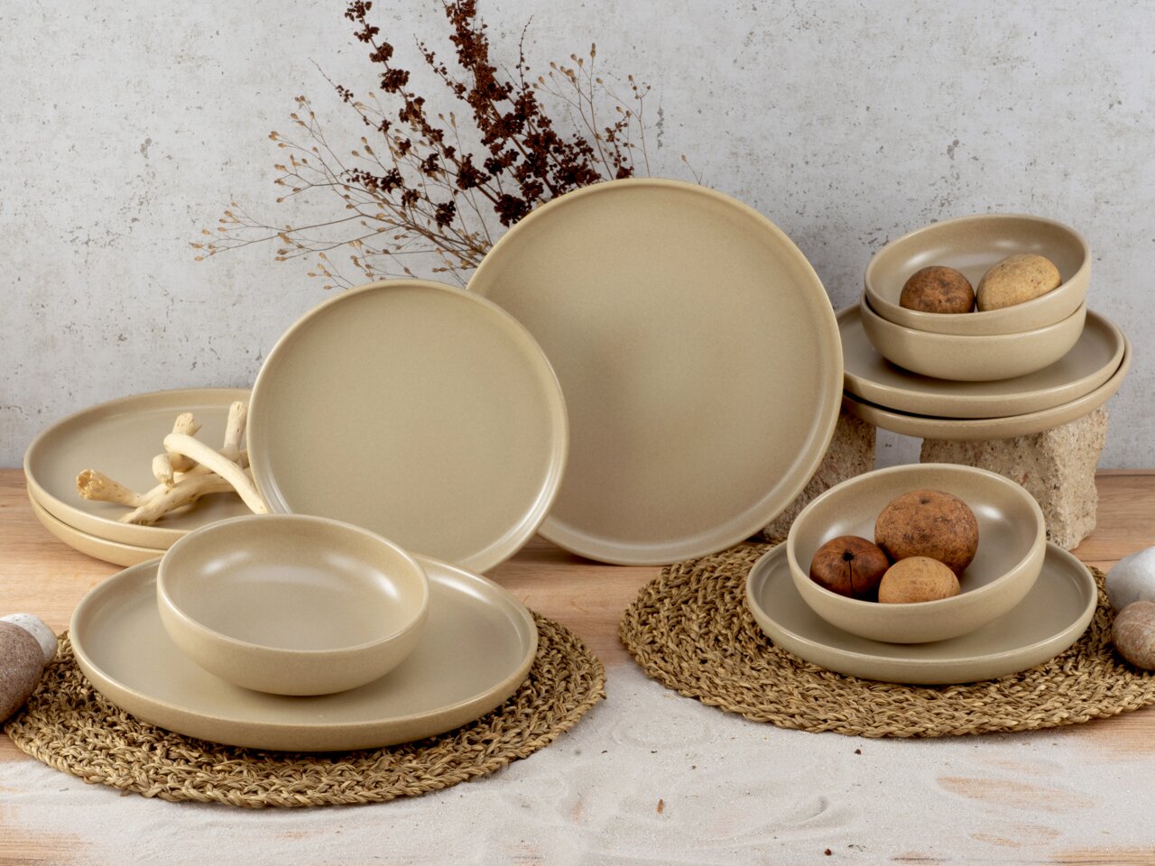 Beiges 12-teiliges Tellerset aus Keramik, bestehend aus flachen und tiefen Tellern sowie Schalen, auf einem Tisch mit natürlicher Dekoration, seitliche Perspektive.