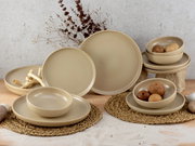 Beiges 12-teiliges Tellerset aus Keramik, bestehend aus flachen und tiefen Tellern sowie Schalen, auf einem Tisch mit natürlicher Dekoration, seitliche Perspektive.