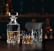 Elegantes Barset Etna 7-tlg. mit Kristallkaraffe und zwei Gläsern, gefüllt mit Whisky, auf einem dunklen Tisch vor unscharfem Hintergrund. Perspektive: seitlich.