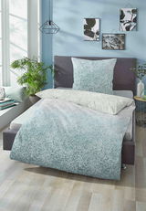 Bettwäsche-Set aus Satin in sanften Blau- und Grautönen auf einem modernen Bett, fotografiert aus einer seitlichen Perspektive in einem hellen, stilvollen Schlafzimmer.