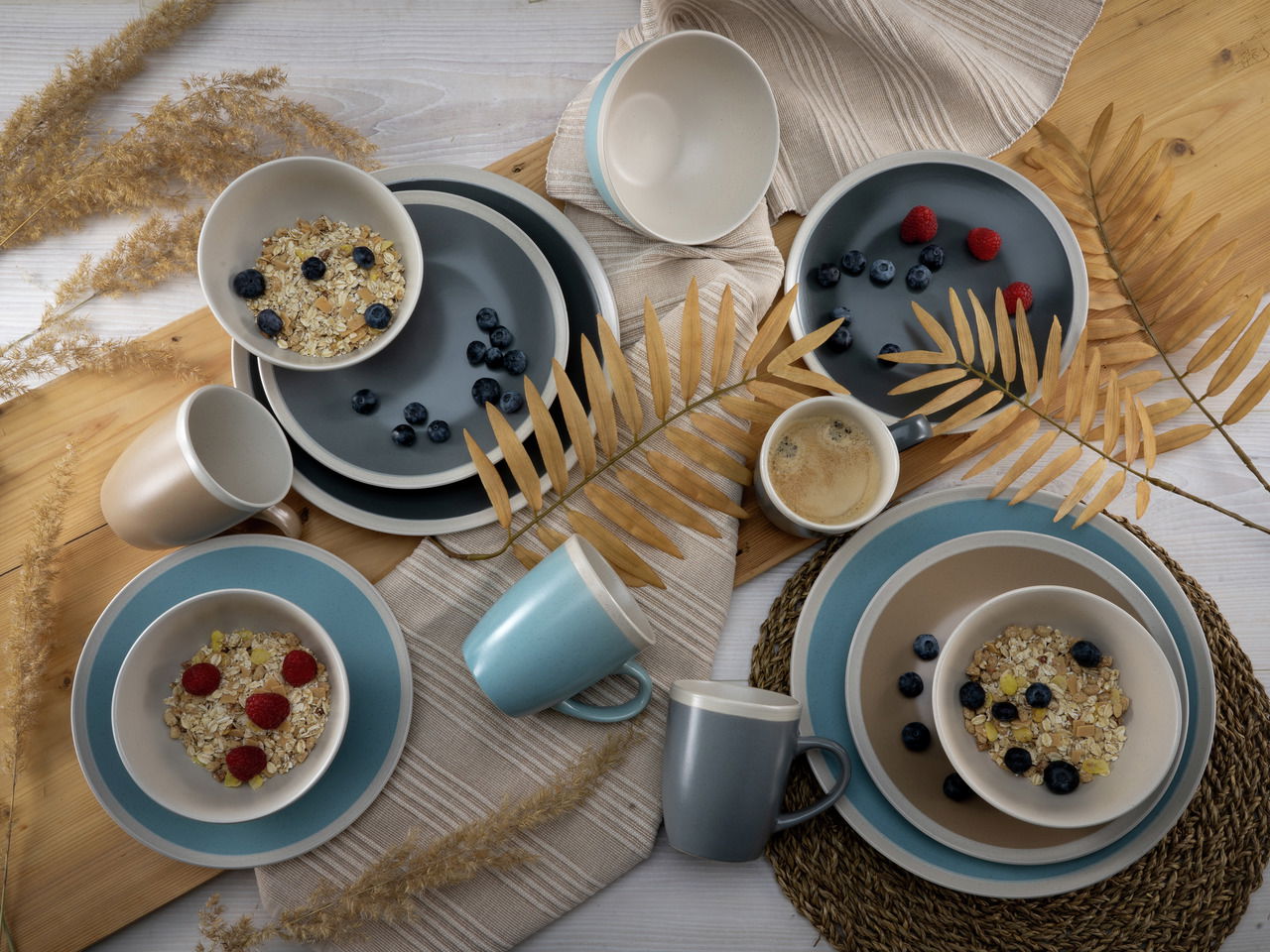 Vogelperspektive auf ein stilvolles Kombiservice-Set 'Nordic Living' mit Tellern, Schalen und Tassen in sanften Blau- und Beigetönen, dekoriert mit Müsli und Beeren.