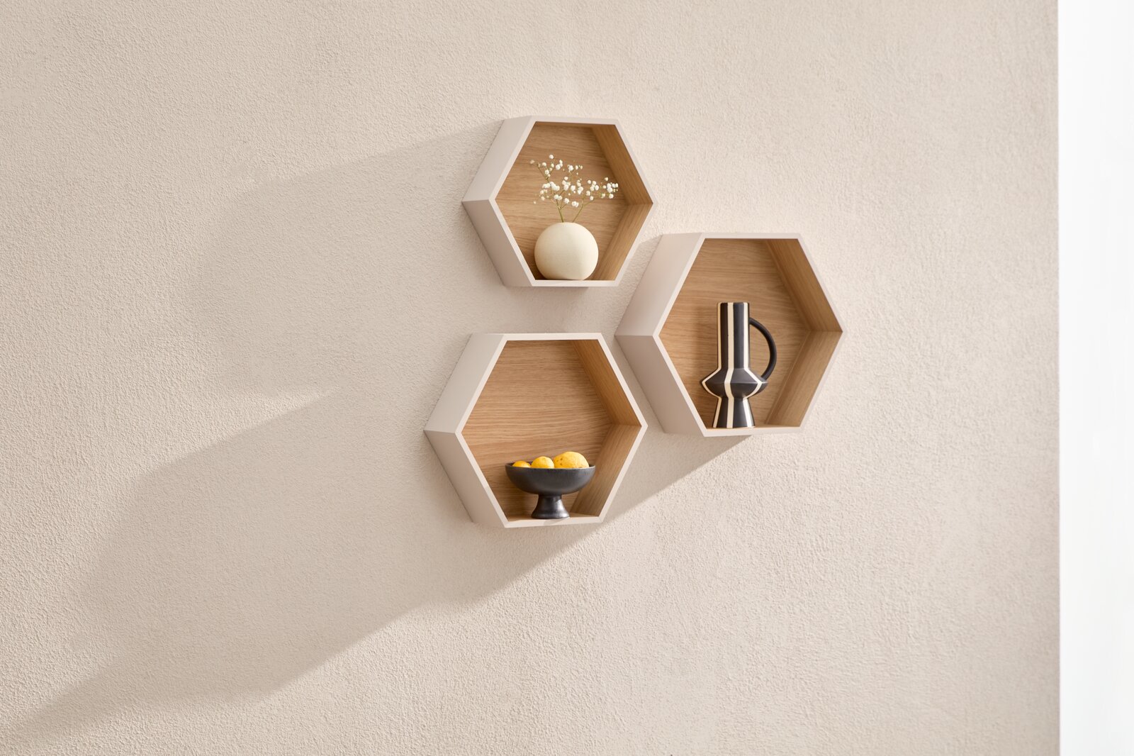 Drie zeshoekige wandplanken met witte randen en een houtlook interieur, decoratief gevuld met vazen en een schaal, schuin van voren bekeken.