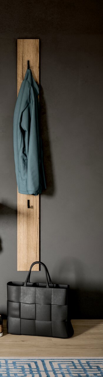 Schmale Garderobenleiste aus hellem Holz mit zwei schwarzen Haken, daran hängt eine blaue Jacke; unten steht eine schwarze geflochtene Tasche vor grauer Wand, Frontansicht.