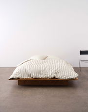 Bett mit gestreifter Bettwäsche in Beige und Weiß, frontal fotografiert, auf einem niedrigen Holzrahmen.