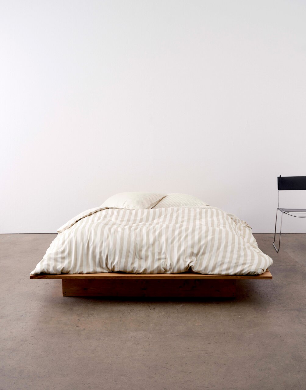 Bett mit gestreifter Bettwäsche in Beige und Weiß, frontal fotografiert, auf einem niedrigen Holzrahmen.