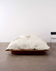 Bett mit gestreifter Bettwäsche in Beige und Weiß, frontal fotografiert, auf einem niedrigen Holzrahmen.
