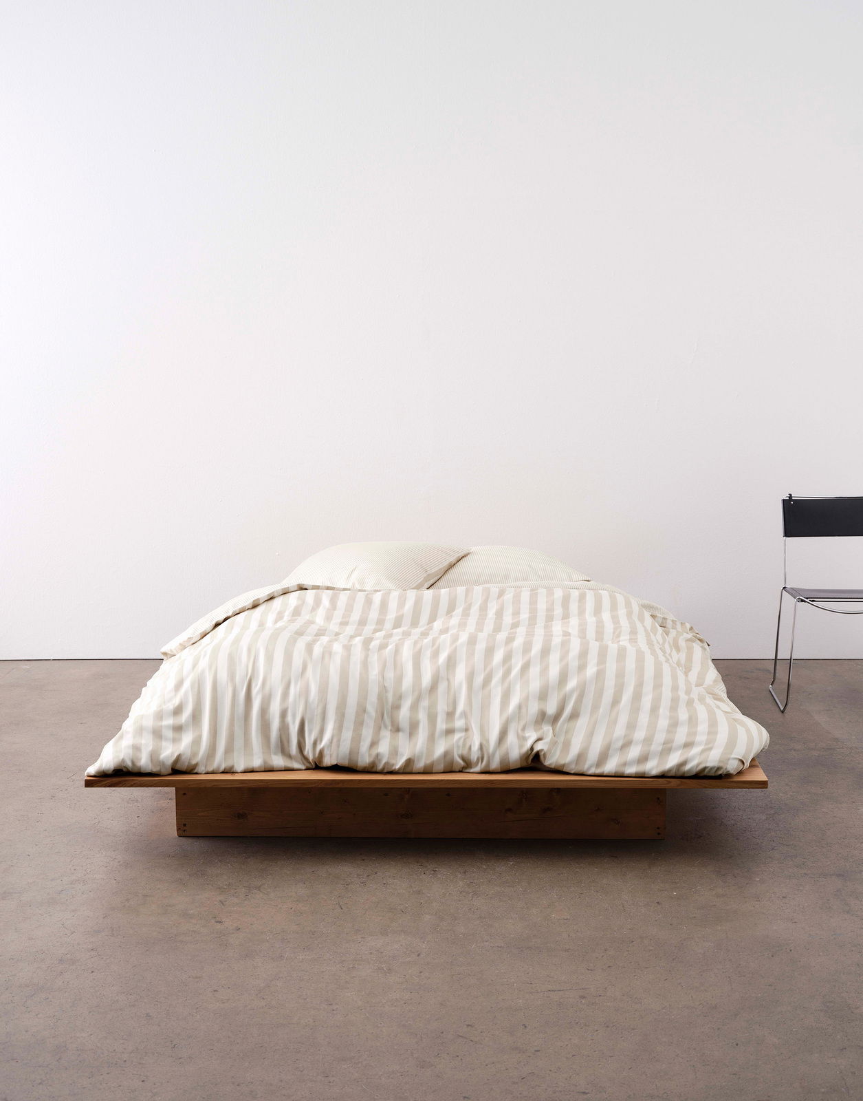 Bett mit gestreifter Bettwäsche in Beige und Weiß, frontal fotografiert, auf einem niedrigen Holzrahmen.