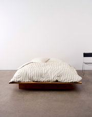 Bed met gestreept beddengoed in beige en wit, van voren gefotografeerd, op een laag houten frame.