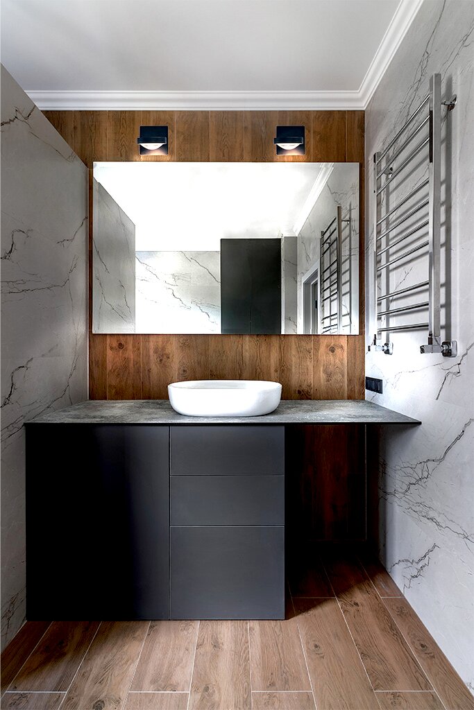 Moderne LED-Wandleuchte SOLO PUNTO - DOWN über einem großen Spiegel in einem stilvollen Badezimmer mit Holz- und Marmorelementen, frontal betrachtet.