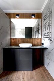 Moderne LED-Wandleuchte SOLO PUNTO - DOWN über einem großen Spiegel in einem stilvollen Badezimmer mit Holz- und Marmorelementen, frontal betrachtet.