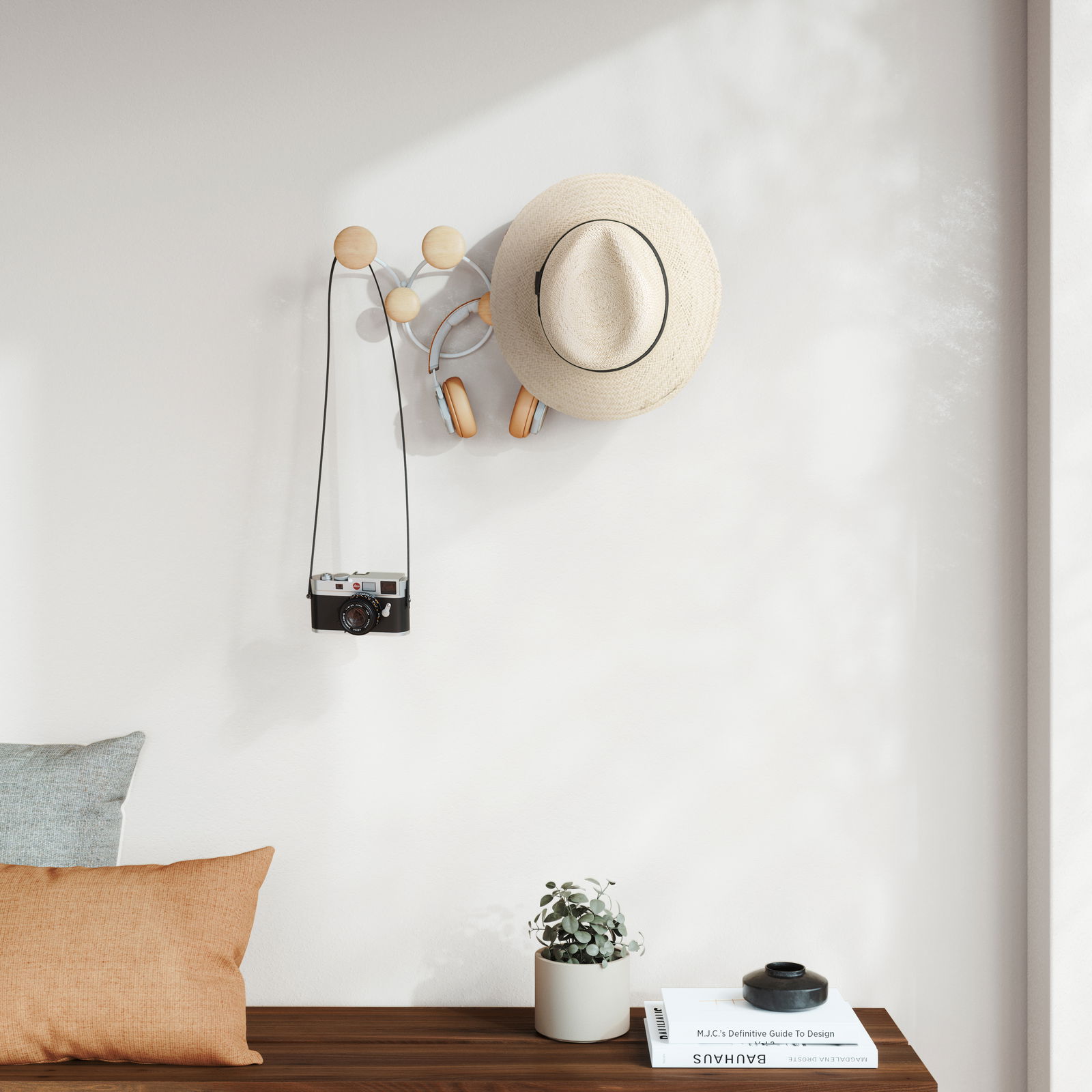 Wandgarderobe mit runden Holzhaken, an der ein Hut, Kopfhörer und eine Kamera hängen, aus seitlicher Perspektive fotografiert.