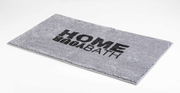 Grauer Badteppich mit der Aufschrift 'HOME BATH', schräg von oben fotografiert.