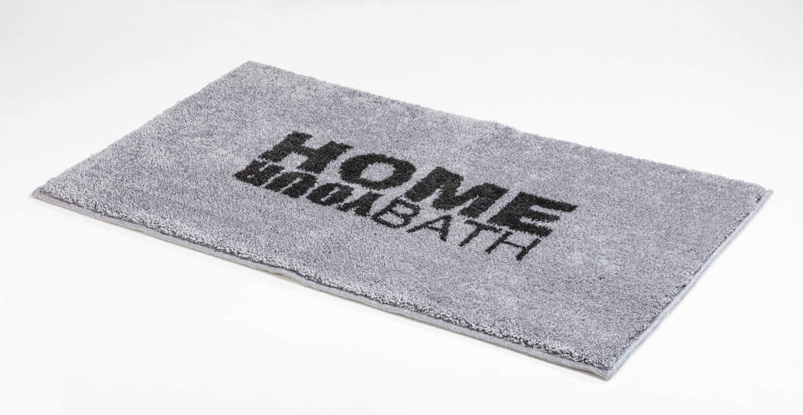 Grauer Badteppich mit der Aufschrift 'HOME BATH', schräg von oben fotografiert.