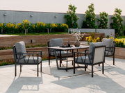 Een moderne tuinset met vier fauteuils en een tafel op een terras, omringd door bloeiende planten. Aanzicht van schuin vooraan.