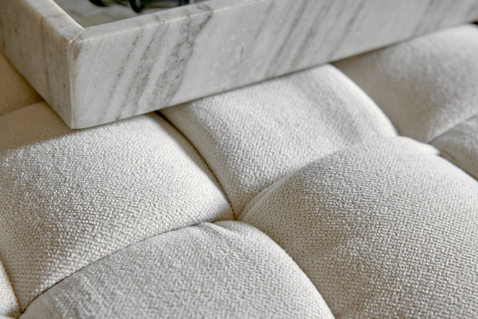 Nahaufnahme eines gepolsterten Hockers mit weißem Stoffbezug und einer Marmorplatte darauf, von oben betrachtet.