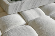 Close-up van een gestoffeerde kruk met een witte stoffen bekleding en een marmeren blad erop, gezien van bovenaf.
