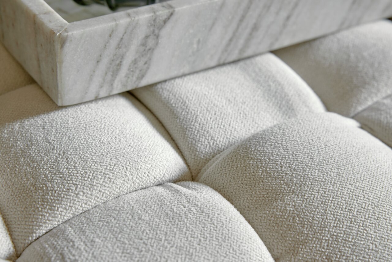 Close-up van een gestoffeerde kruk met een witte stoffen bekleding en een marmeren blad erop, gezien van bovenaf.