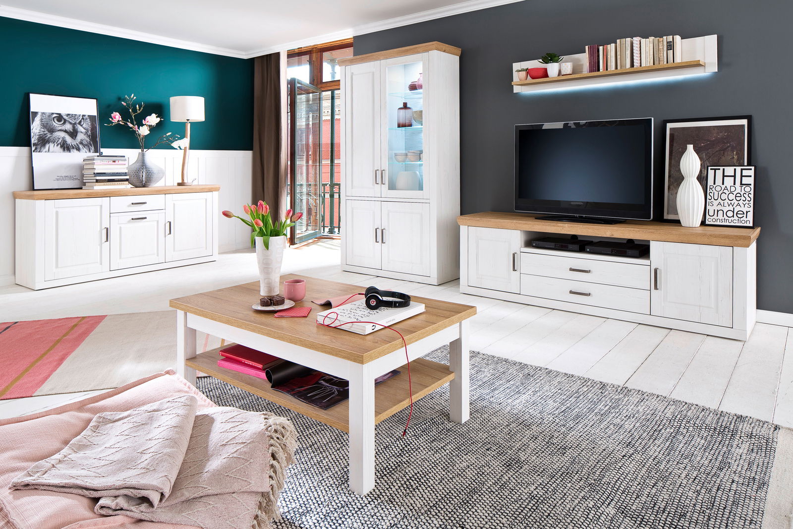 Wohnzimmer mit moderner Wandkombination in Weiß und Holzoptik, bestehend aus TV-Schrank, Vitrine und Regal, aus der Perspektive des Raumes betrachtet.
