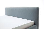 Seitliche Ansicht eines grauen Polsterbetts mit schlichtem Kopfteil.