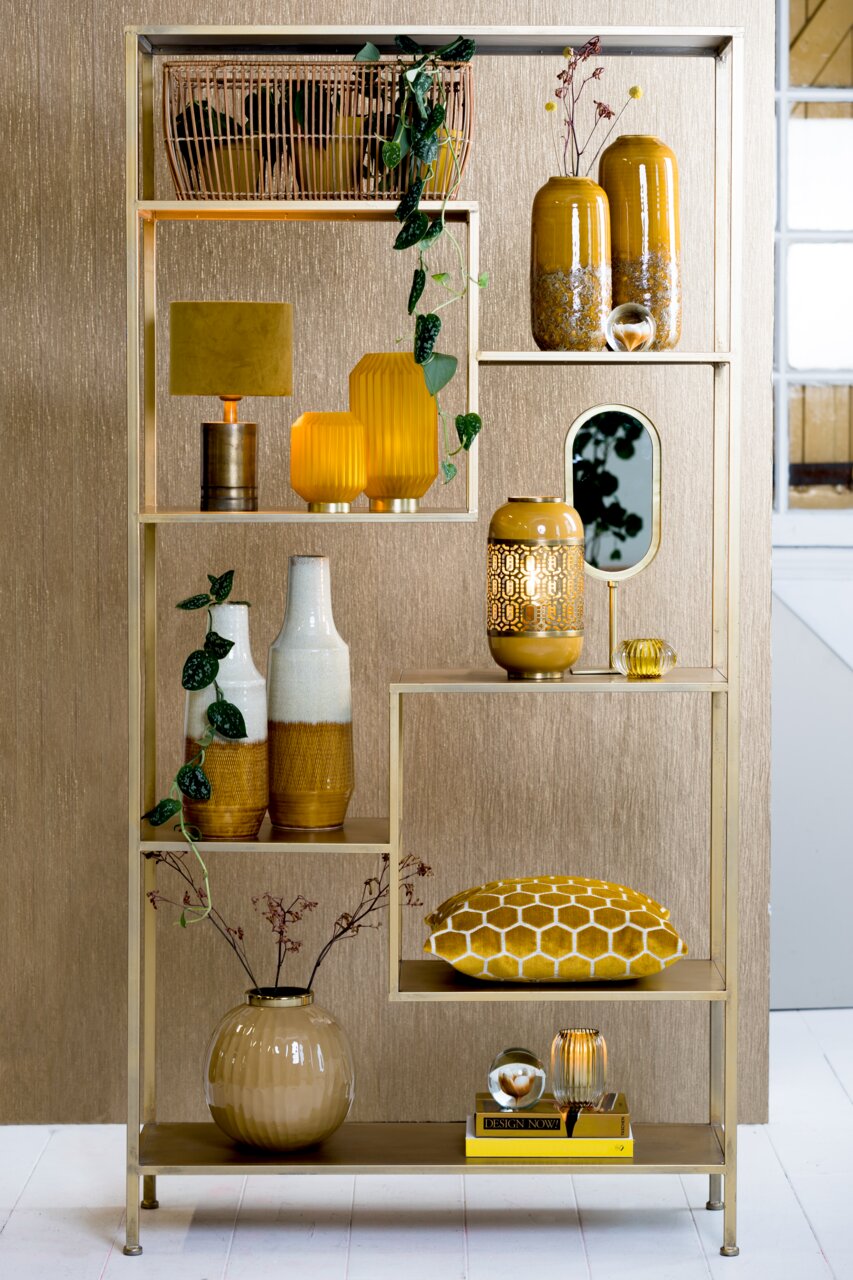 Een open plank met gouden en gele decoratievoorwerpen, waaronder vazen, kussens en planten, in een moderne woonruimte. Vooraanzicht.