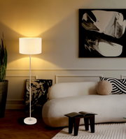 Moderne staande lamp met witte lampenkap in een stijlvol ingerichte woonkamer, gezien vanaf de zijkant.