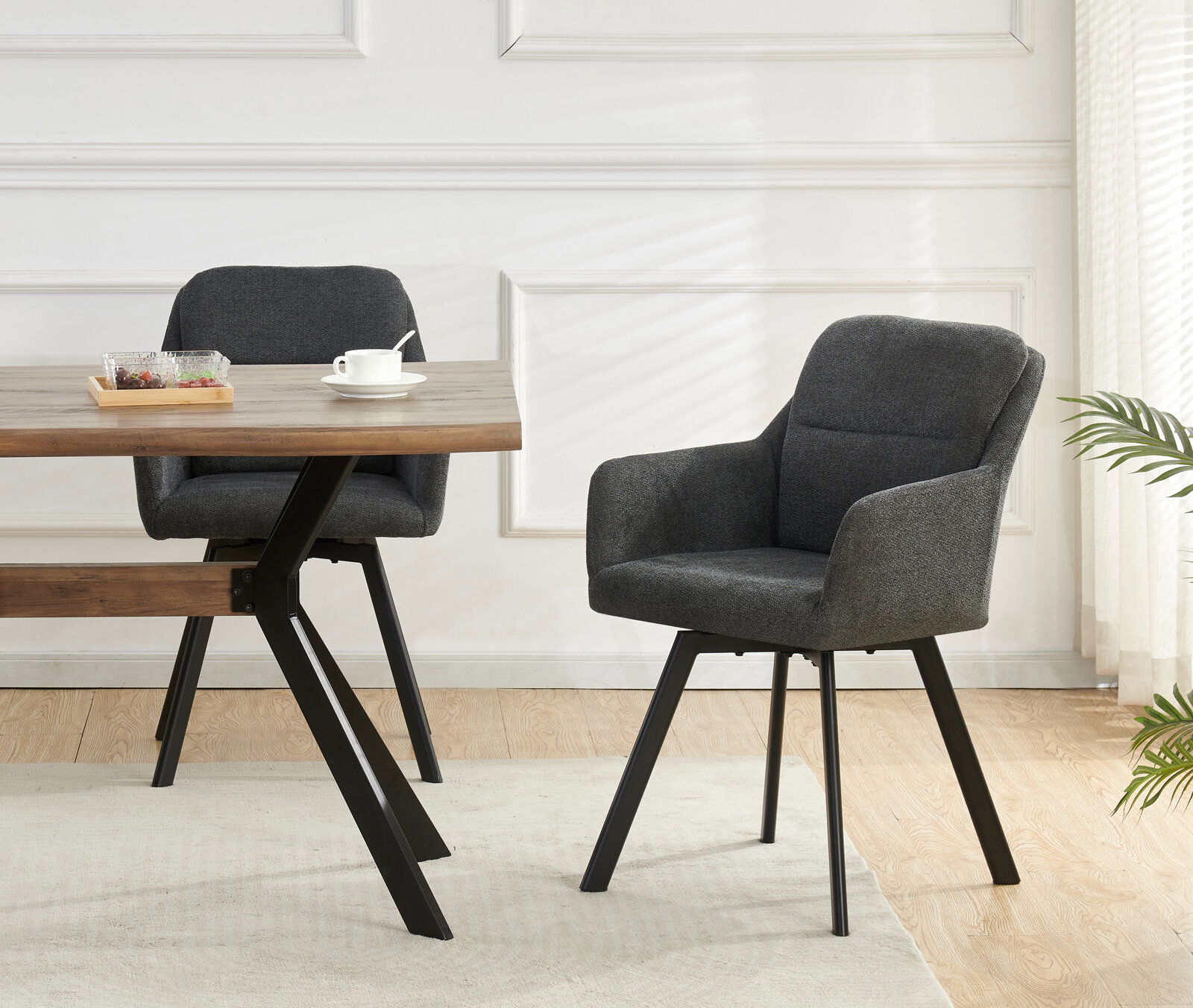 Dunkelgrauer, gepolsterter Esszimmer-Armlehnstuhl mit schwarzem Metallgestell neben Holztisch in hellem Raum, Perspektive: leicht seitliche Frontansicht