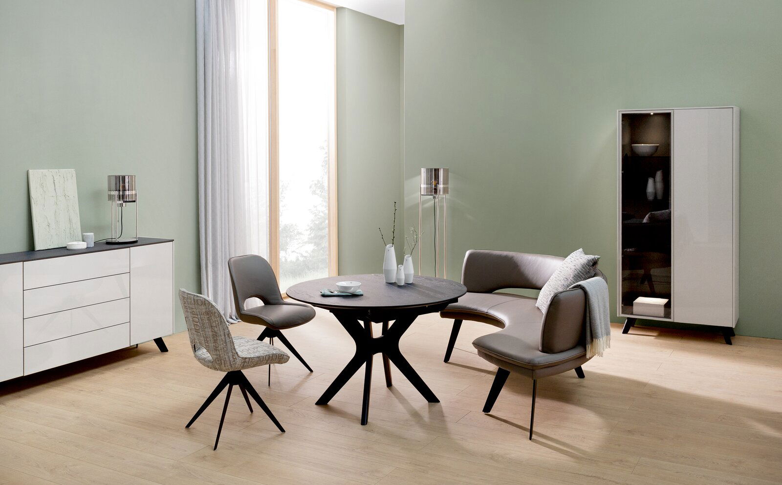 Moderner Esstisch in einem stilvollen Wohnzimmer mit grüner Wand, umgeben von eleganten Stühlen und einem Sofa, aus seitlicher Perspektive betrachtet.