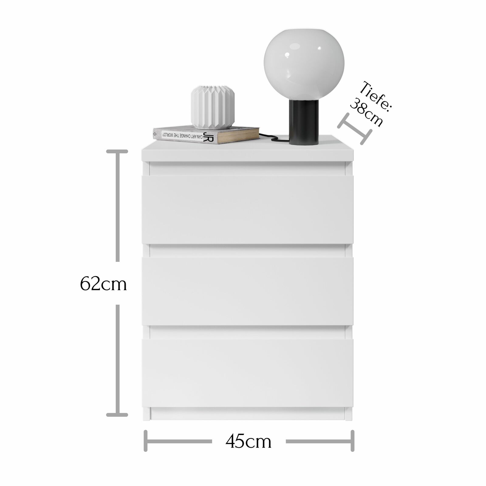 Weiße Nachtkommode mit drei Schubladen, darauf eine Lampe und ein Buch, frontale Ansicht, Maße: 62cm hoch, 45cm breit, 38cm tief.