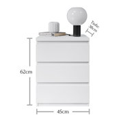 Weiße Nachtkommode mit drei Schubladen, darauf eine Lampe und ein Buch, frontale Ansicht, Maße: 62cm hoch, 45cm breit, 38cm tief.