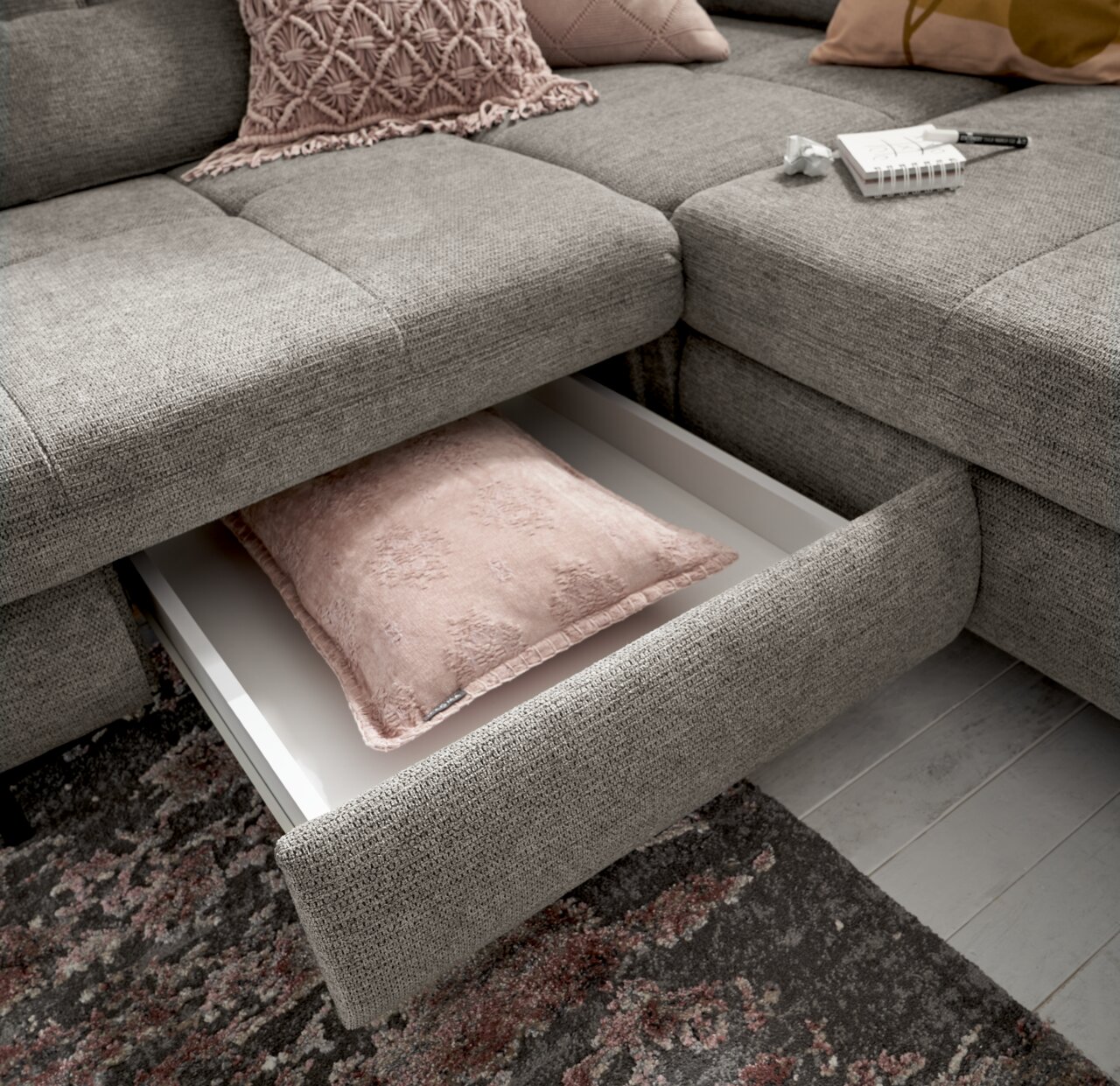 Graues Ecksofa mit herausgezogenem Schubfach, das ein rosa Kissen enthält. Perspektive von oben.