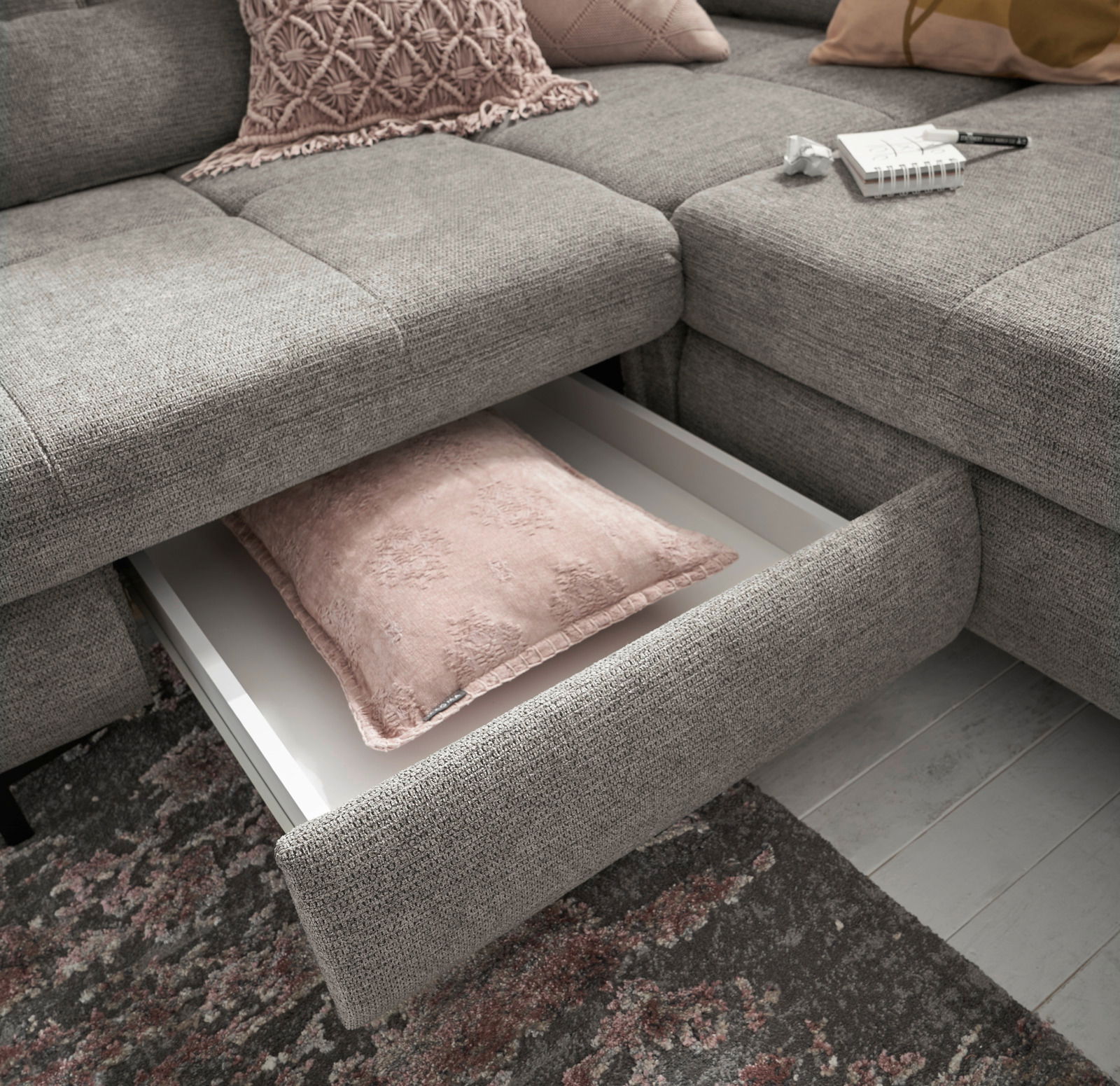 Graues Ecksofa mit herausgezogenem Schubfach, das ein rosa Kissen enthält. Perspektive von oben.