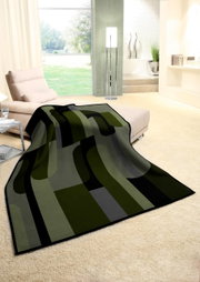 Moderne Wohndecke in Grün- und Grautönen mit geometrischem Muster, drapiert über einem Sofa in einem hellen Wohnzimmer mit Blick auf den Garten.