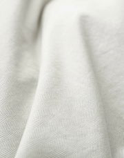 Nahaufnahme einer Bettwäsche mit dezentem Fischgrätenmuster in sanften Grautönen, aus seitlicher Perspektive aufgenommen.