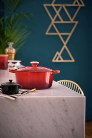 Roter Le Creuset Bräter, rund, 24 cm, auf einem Marmortisch in einer modernen Küche, seitliche Perspektive