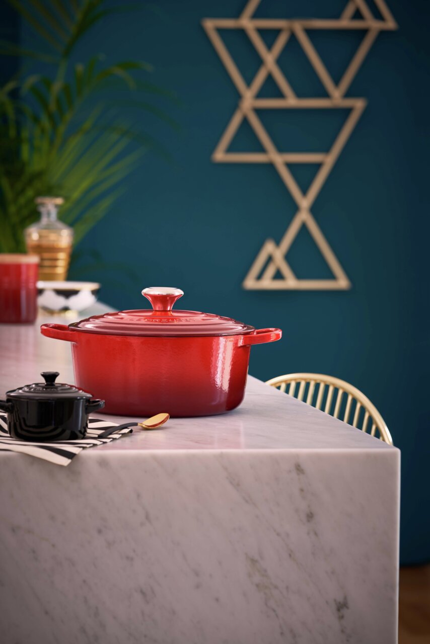 Roter Le Creuset Bräter, rund, 24 cm, auf einem Marmortisch in einer modernen Küche, seitliche Perspektive