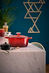 Roter Le Creuset Bräter, rund, 24 cm, auf einem Marmortisch in einer modernen Küche, seitliche Perspektive