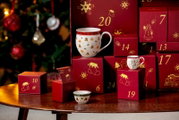Festlicher Porzellan-Adventskalender mit roten, goldverzierten Geschenkboxen sowie Tasse, Miniaturkännchen und Schälchen mit weihnachtlichem Dekor, aus frontaler Perspektive arrangiert.