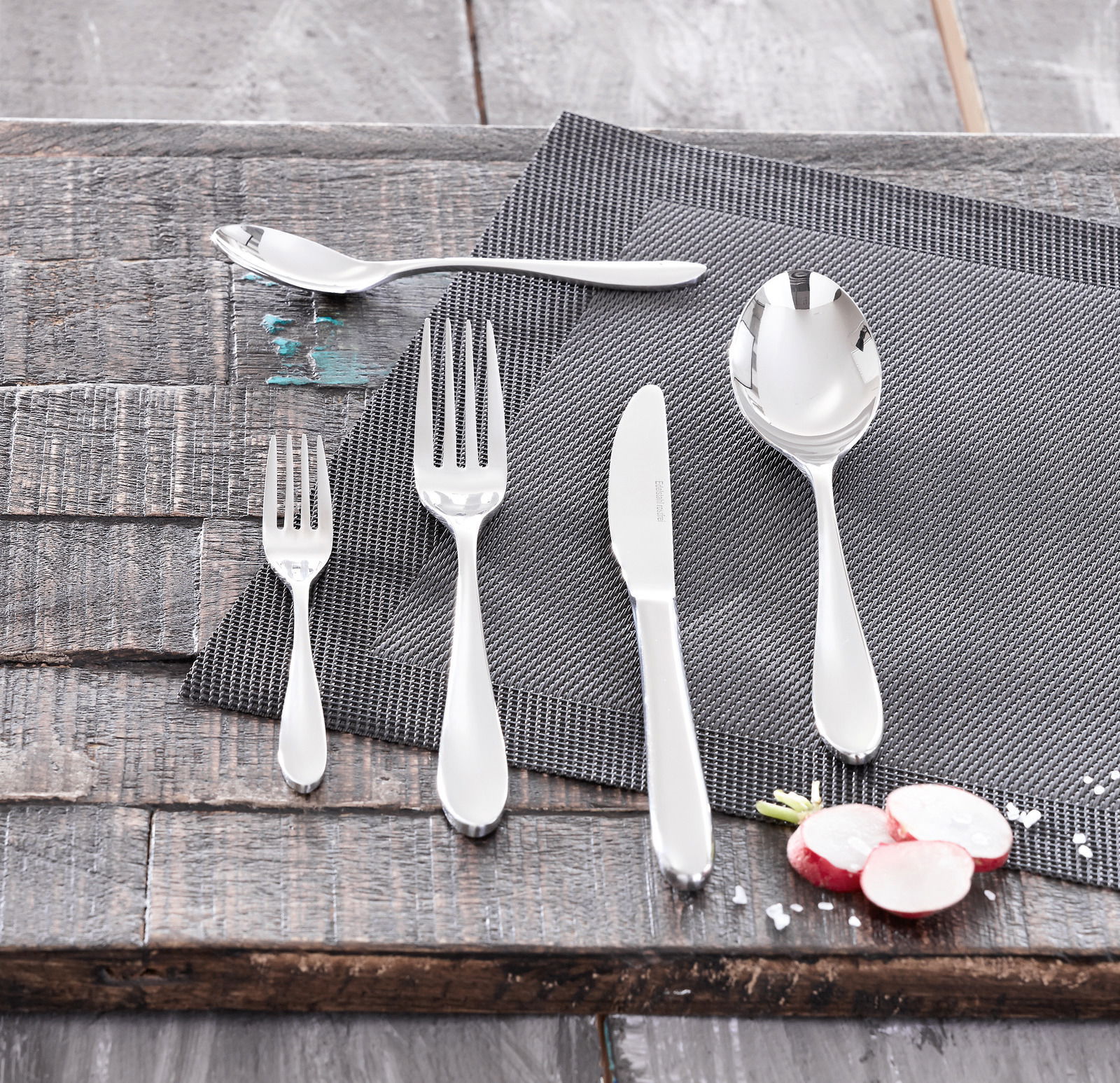 Besteckset bestehend aus Messer, Gabel, Löffel und Teelöffel auf einem grauen Platzdeckchen, von oben fotografiert.