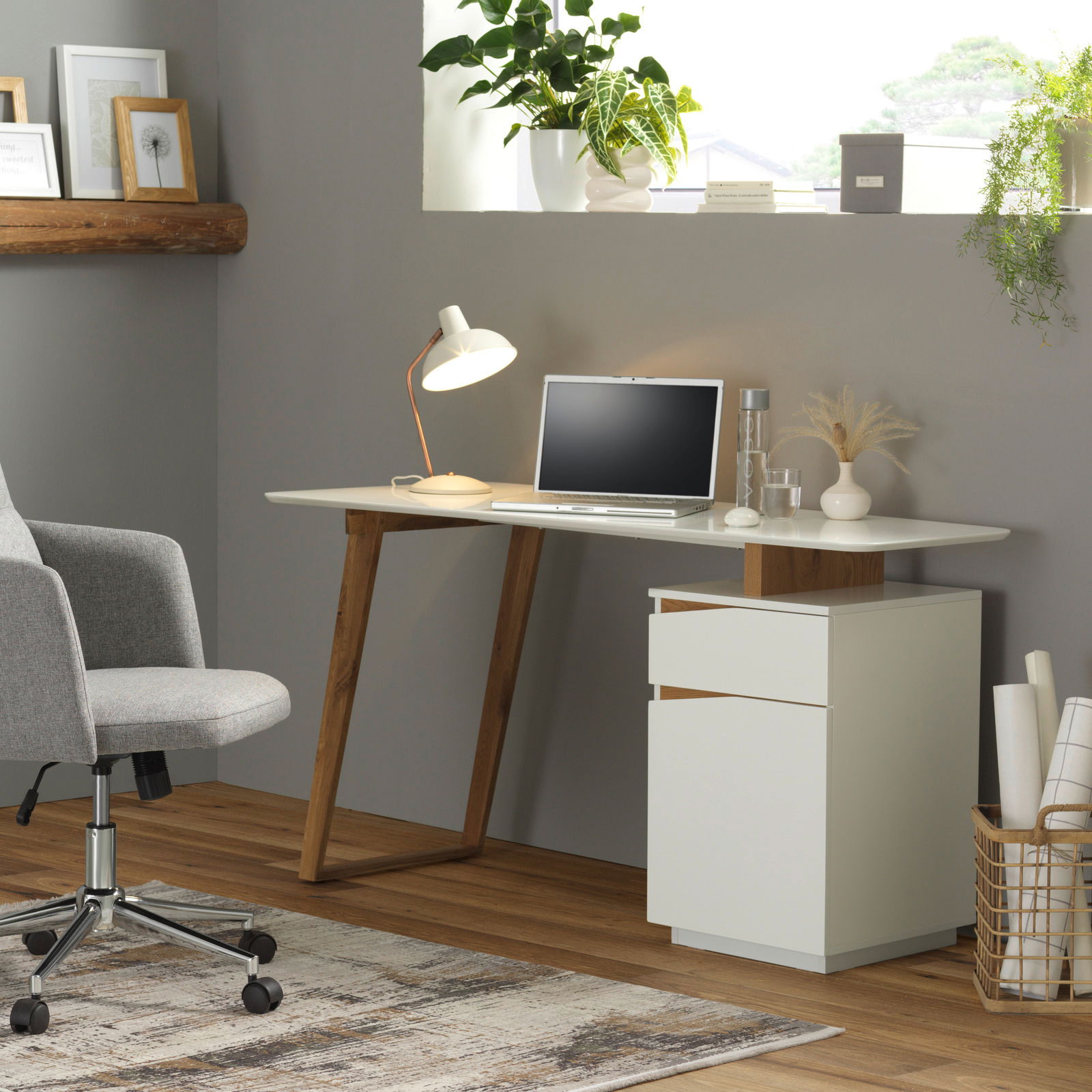 Moderner Schreibtisch mit weißer Tischplatte und Holzbeinen, seitlich mit Schubladenelement, aus der Perspektive eines gemütlichen Home-Office.