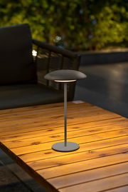 Moderne Akku-Tischleuchte SARDINIA auf einem Holztisch, seitliche Perspektive, ideal für stimmungsvolle Beleuchtung im Freien.