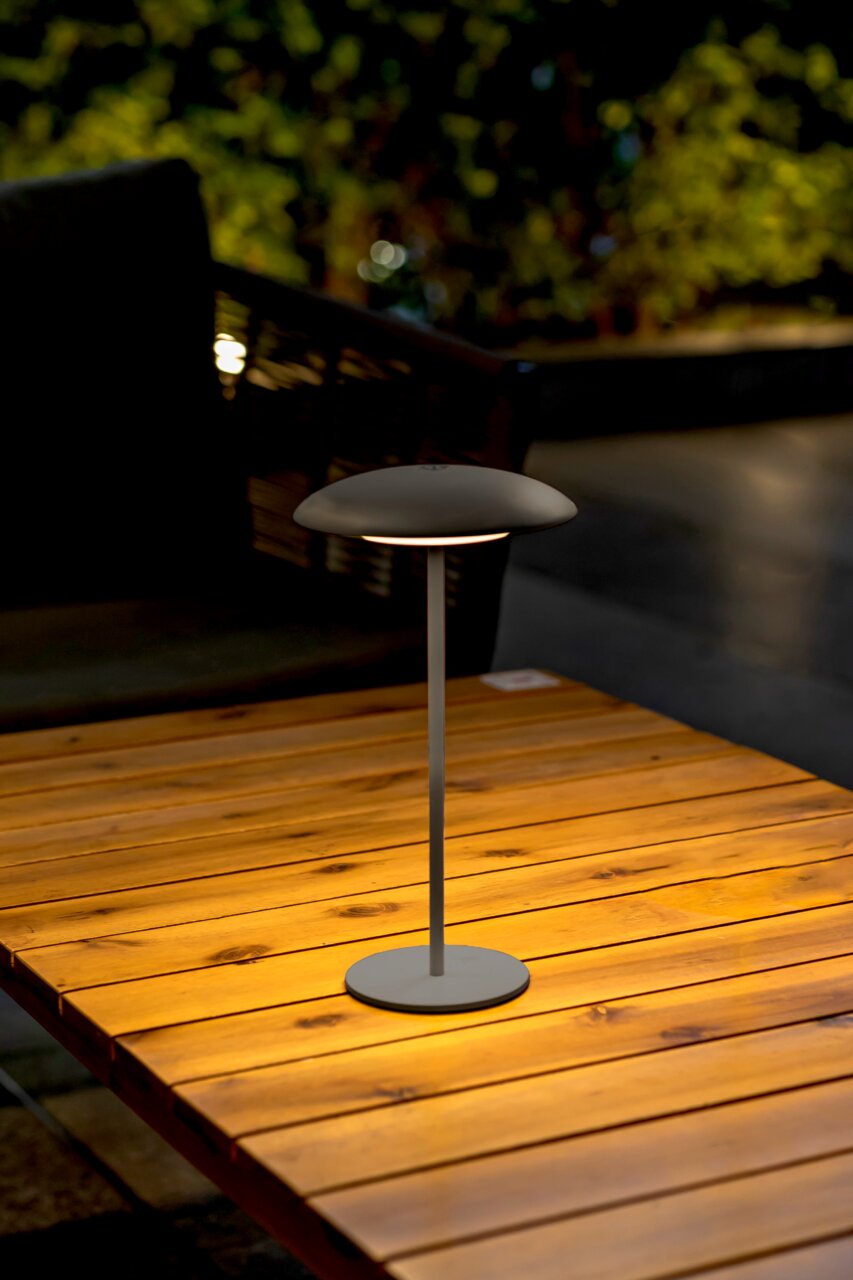 Moderne Akku-Tischleuchte SARDINIA auf einem Holztisch, seitliche Perspektive, ideal für stimmungsvolle Beleuchtung im Freien.