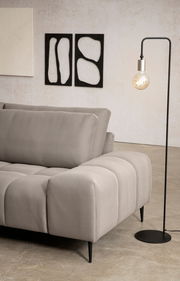 Rückansicht einer modernen Longchairkombination in grauem Stoff mit schwarzem Metallfuß, neben einer Stehlampe und abstrakter Wandkunst.