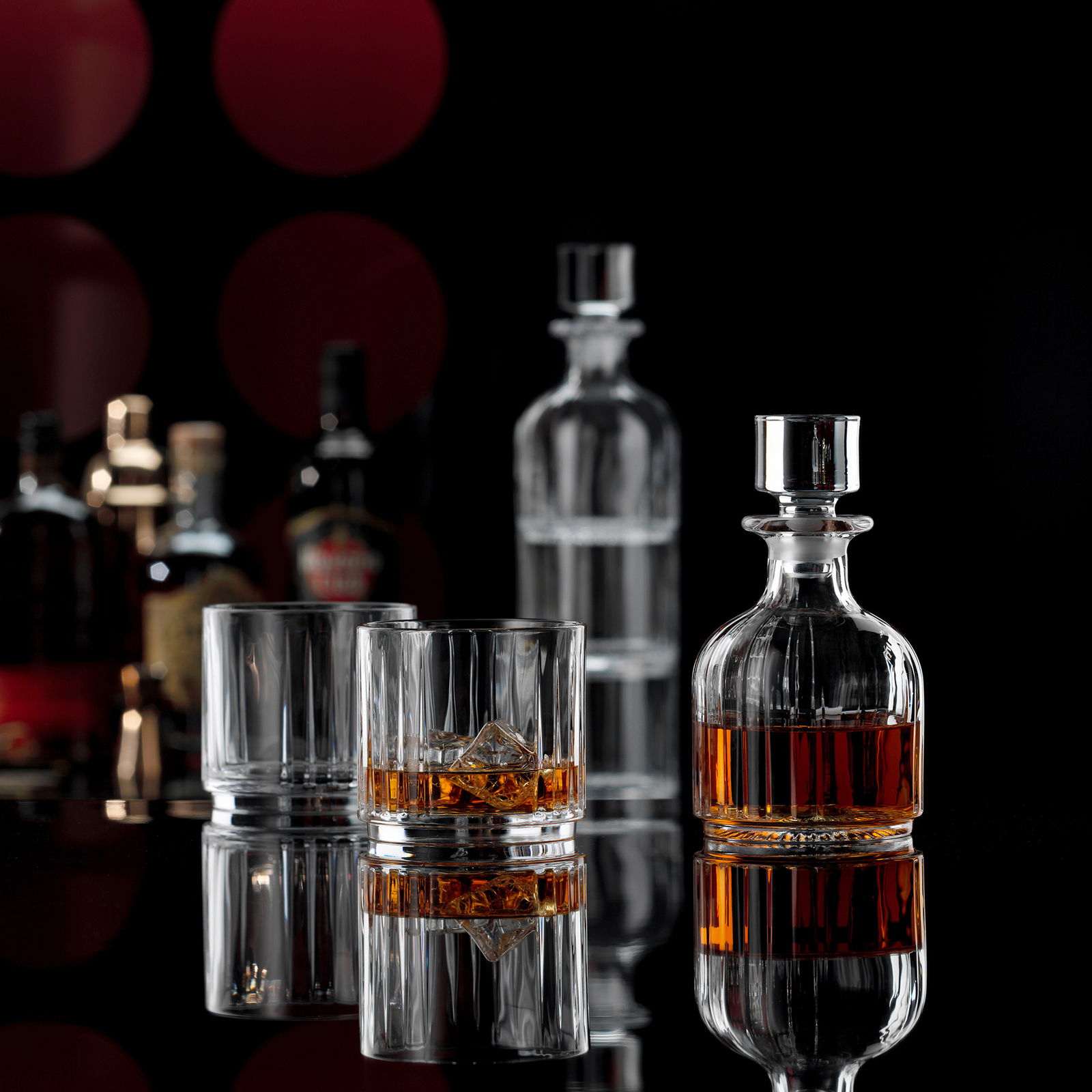 Elegantes Whisky-Set mit Karaffe und zwei Gläsern, gefüllt mit Whisky und Eiswürfeln, auf schwarzem Hintergrund mit reflektierender Oberfläche, seitliche Perspektive.
