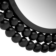 Nahaufnahme eines runden Spiegels mit einem dekorativen schwarzen Rahmen aus kugelförmigen Elementen, perspektivisch von der Seite aufgenommen.
