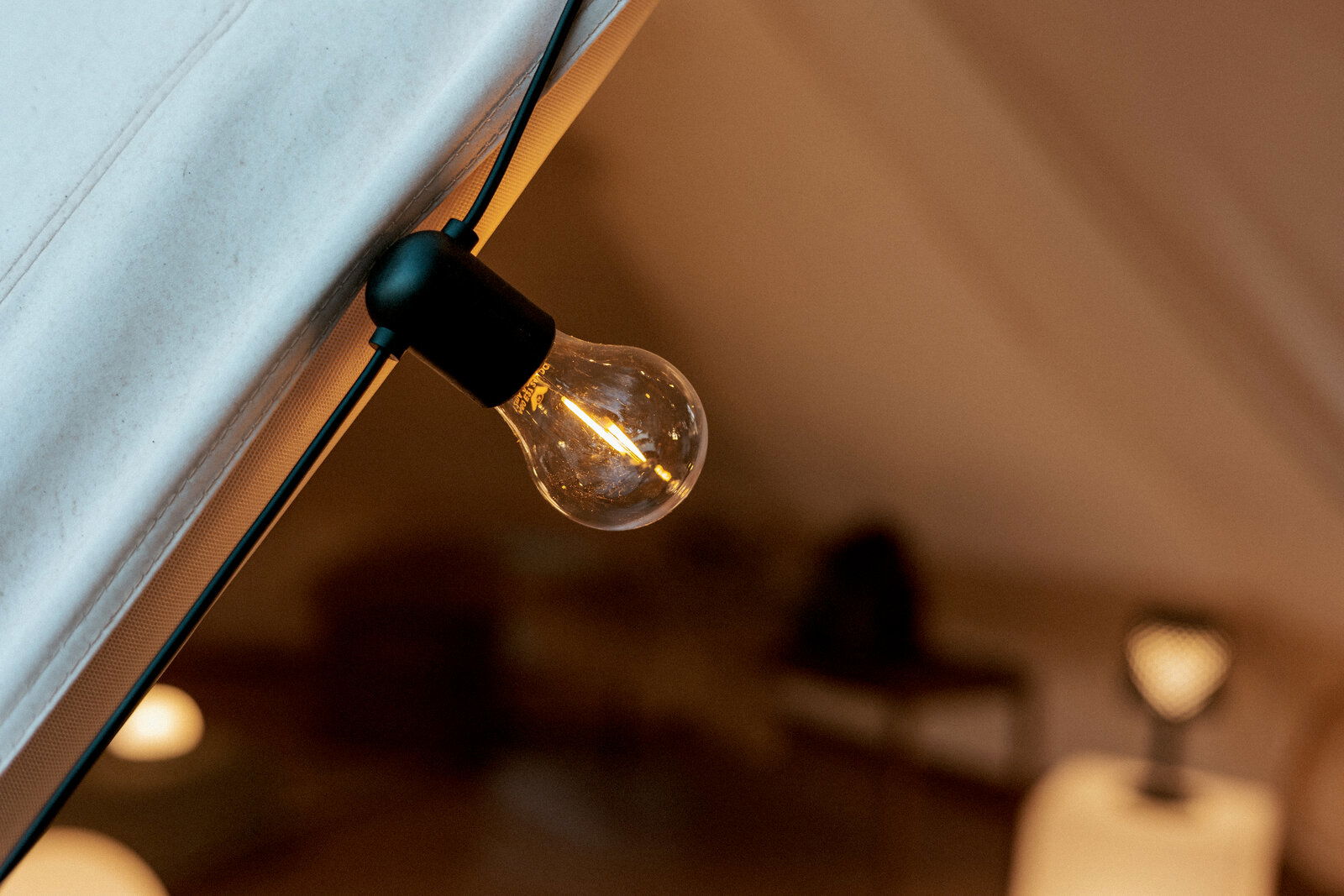 Nahaufnahme einer warm leuchtenden Glühbirne an einer Lichterkette im Zeltinneren, schräg von unten fotografiert