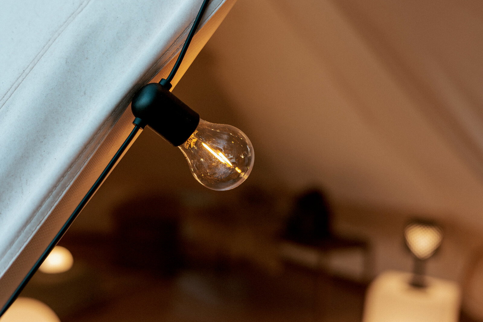 Nahaufnahme einer warm leuchtenden Glühbirne an einer Lichterkette im Zeltinneren, schräg von unten fotografiert