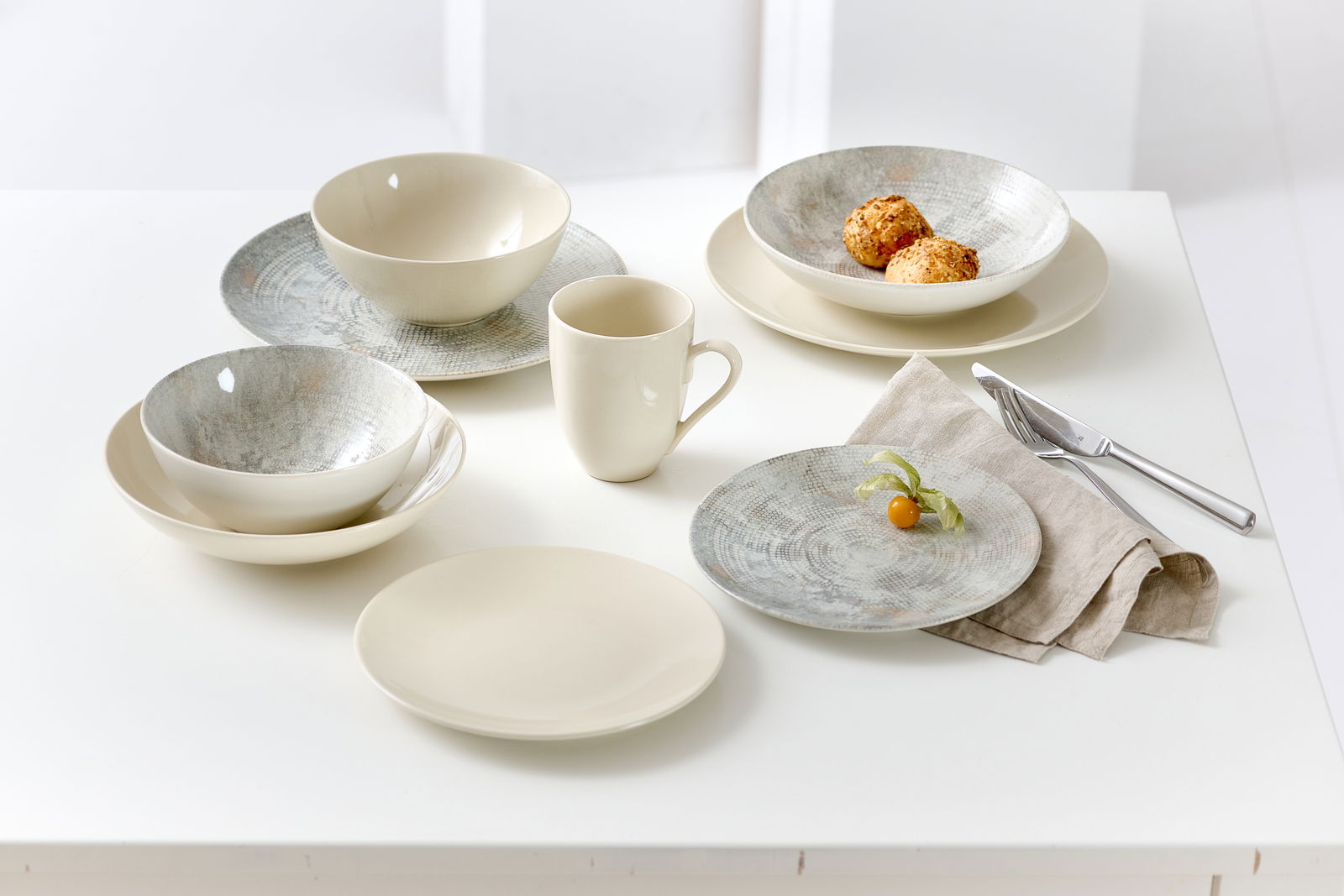 Tischgedeck mit verschiedenen Schalen und Tellern in einem eleganten, cremefarbenen Design, fotografiert aus einer leicht erhöhten Perspektive.