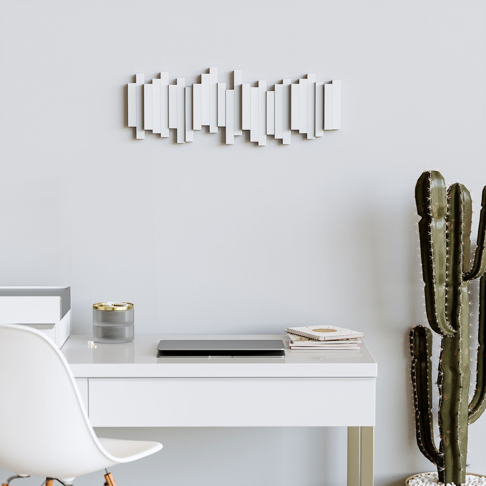 Moderne Wandgarderobe in geometrischem Design, frontal an einer hellen Wand über einem Schreibtisch mit Dekorationen und einem Kaktus platziert.