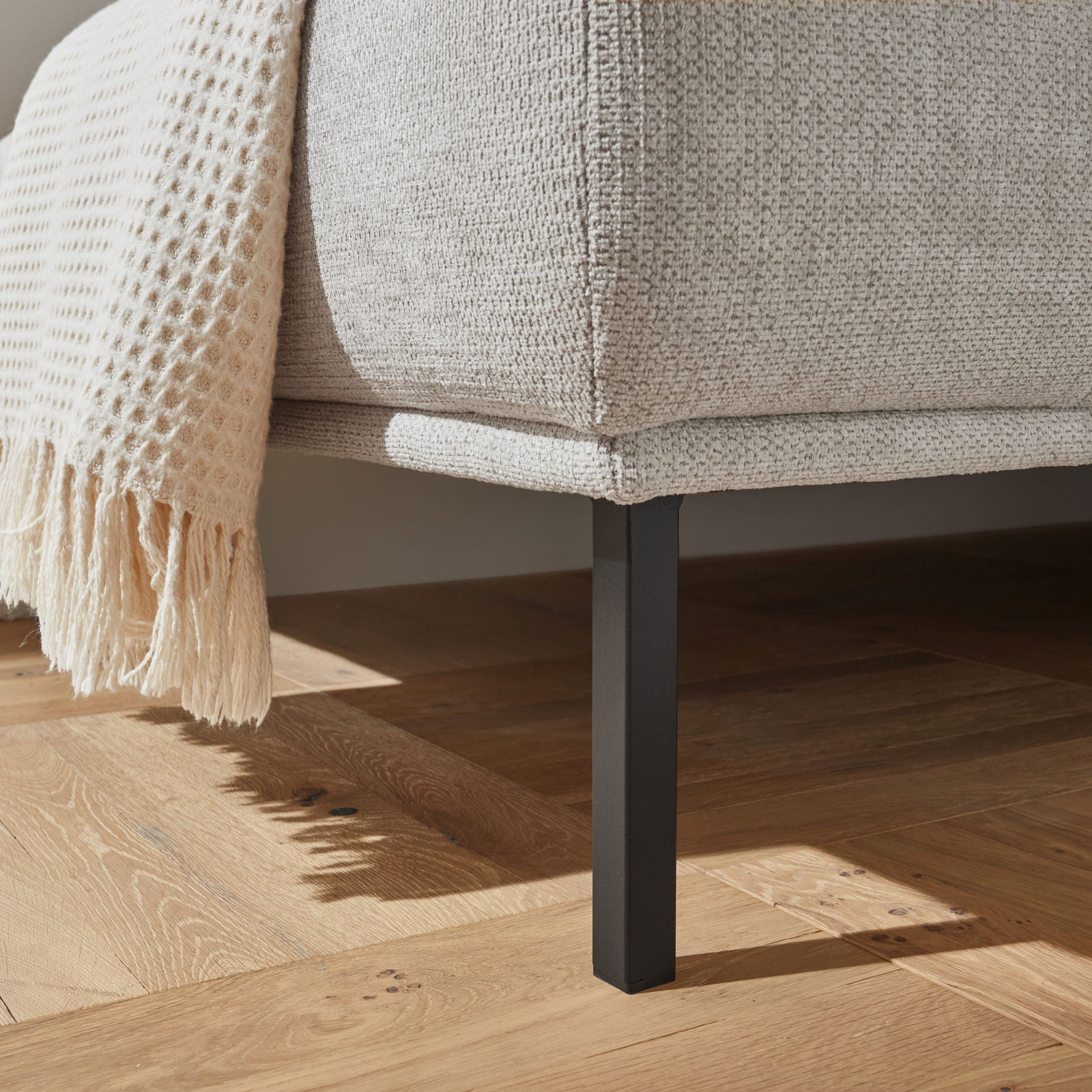 Nahaufnahme eines Hockers mit hellgrauem Stoffbezug und schwarzem Metallbein, seitliche Perspektive