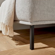 Nahaufnahme eines Hockers mit hellgrauem Stoffbezug und schwarzem Metallbein, seitliche Perspektive